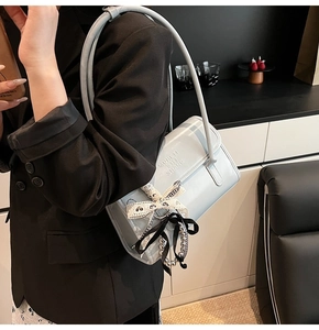 Detalle de bolso bandolera azul claro con colgante de lazo de encaje y logotipo grabado