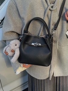 Elegante bolso tipo cubo de cuero negro con cierre plateado y un colgante de peluche
