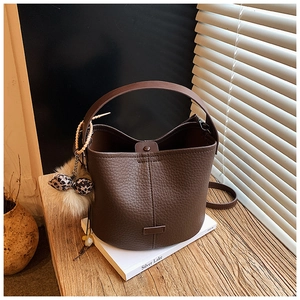 Detail of dark brown lychee grain leather bucket bag with leopard bow puff keychain