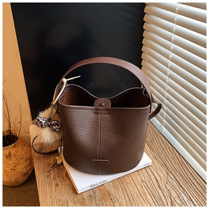 Detail of dark brown bucket bag featuring pebble leather texture and a leopard bow charm