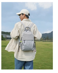 Outdoor back view of a person wearing a light grey casual nylon backpack on a lawn