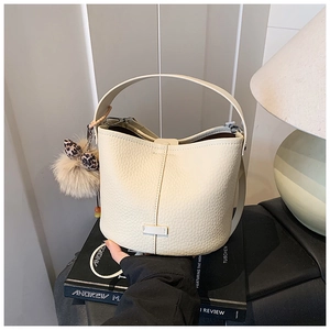 Detail of cream bucket bag in lychee leather with plush leopard bow charm on book
