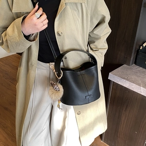Detail view of black lychee grain leather bucket bag with leopard print pom pom charm