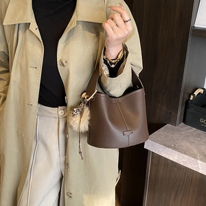 Close-up of dark brown lychee texture leather bucket bag with plush pompom charm detail