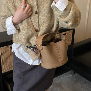 Detail of a brown lychee pattern leather bucket bag with a plush charm and metal rings