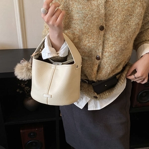 Detail of minimalist cream bucket bag with litchi grain texture and plush pom pom charm
