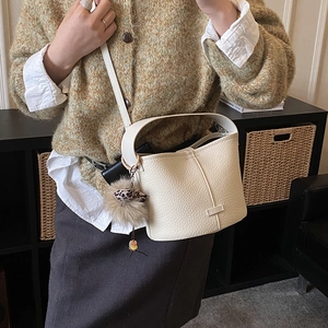 Detail view of cream white bucket bag with pebble leather texture and fuzzy ball charm