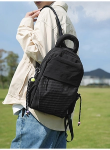 Detail view of black commuter backpack with woven textures and drawstring accents outdoors