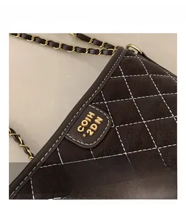 Detail einer dunkelbraunen gesteppten Wildledertasche mit Goldlogo und weißer Naht