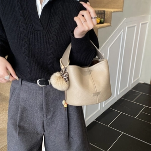Detail view of beige lychee textured leather bucket bag with decorative keychain charms