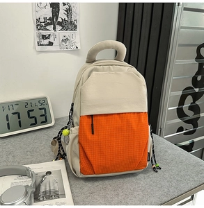 Detail of beige and orange backpack with checkered front pocket and tennis ball charm