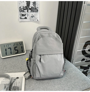 Detail view of a light grey nylon backpack with grid patterns and a small yellow charm