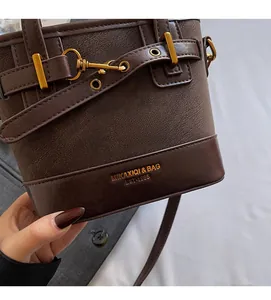 Vista dettagliata della borsa a secchiello marrone scuro con fibbia dorata e logo