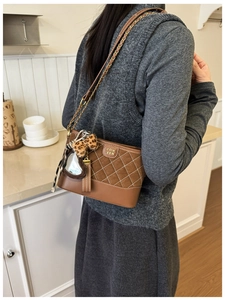 Detailansicht der braunen Stepp-Beuteltasche mit goldener Kette und Anhängern am Modell