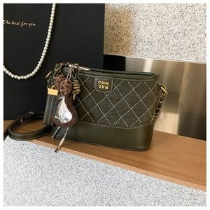 Detail der grünen Stepptasche mit Goldlogo und Leoparden-Herzanhänger auf Holzregal