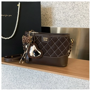 Detail der dunkelbraunen gesteppten Beuteltasche mit Herzanhänger und Leopardenmuster-Accessoire