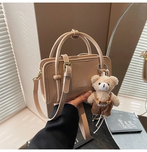 Détail d'un sac bandoulière beige avec poignées, bandoulière réglable et pendentif ourson