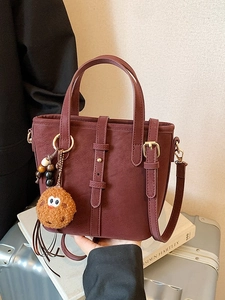 Minimalistische bordeauxrote Beuteltasche mit Lederband und Plüschanhänger auf Buch