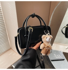 Détail d'un sac à main noir brillant avec dorure et pendentif d'ours en peluche brun