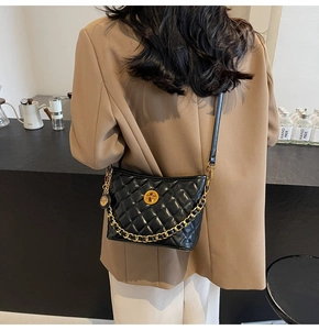 Close-up of quilted black leather crossbody bag with gold chain and round buckle detail