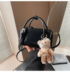 Detail der schwarzen glänzenden Mini-Tasche mit Metalllogo und Plüschbär-Anhänger