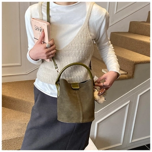 Detail der vintage olivgrünen matten Beuteltasche mit weißen Nähten und Bärenanhänger
