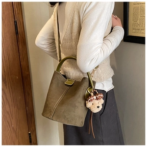 Detailansicht der olivgrünen Wildleder-Eimertasche mit Lederriemen und Plüschbär-Anhänger