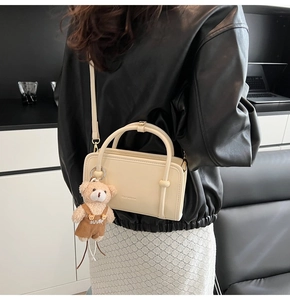 Detailansicht der cremefarbenen quadratischen Handtasche mit Teddybär-Anhänger am Model