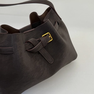 Detail of dark brown suede bucket bag featuring a decorative side knot and gold buckle