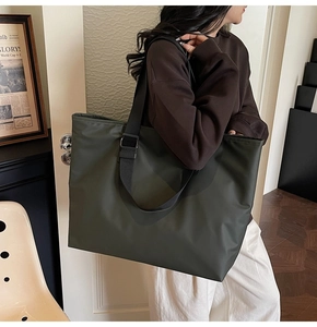 Vue latérale du grand sac cabas vert foncé avec large bandoulière noire sur tenue décontractée