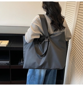 Vue latérale d'un grand sac cabas noir minimaliste porté à l'épaule par un mannequin
