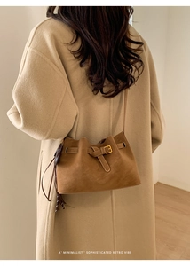 Detail of caramel suede bag featuring metallic buckle and fringe tassels on wool coat