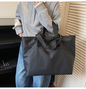 Détail d'un grand sac cabas noir à doubles anses porté par un mannequin dans un bureau
