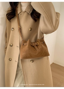 Close-up of brown suede bucket bag with retro metal buckle worn over a beige wool coat