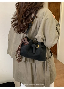 Close-up of black matte bucket bag with gold buckle and brown woven letter tassel detail