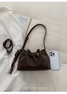 Detail of dark brown suede bucket bag with gold buckle and fringe on linen surface