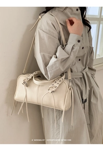 Detail view of cream Boston bag with woven lace-up patterns and long tassel accents
