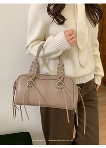 Detail of retro leather bag featuring woven handles, silver rings and long tassels