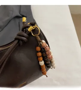 Detalle de bolso de cuero marrón oscuro con colgante de cuentas y anillos dorados