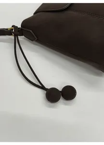 Détail d'un sac bandoulière marron foncé avec breloques à deux boules et texture cuir mat