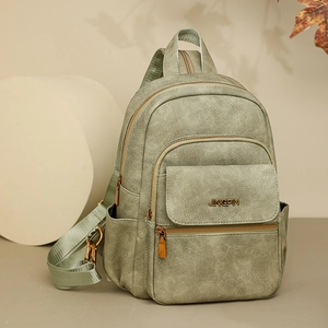 Detail view of sage green multi-pocket backpack with textured faux leather and bronze zippers