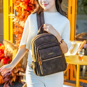 Detail of vintage brown matte backpack showing magnetic flap and metal zippers in outdoor setting