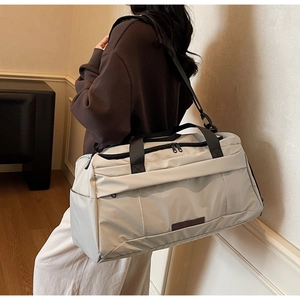 Detail der cremefarbenen Reisetasche mit schwarzen Riemen und praktischen Seitentaschen