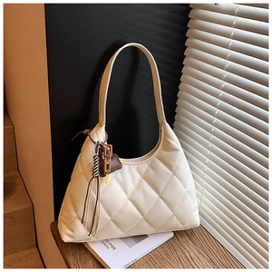 Detail van beige gewatteerde schoudertas met decoratieve hanger op een houten vensterbank