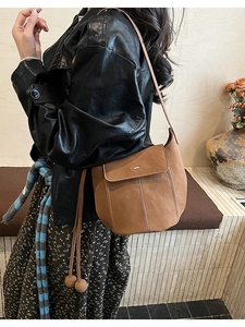 Détail d'un sac seau en daim marron avec surpiqûres blanches et cordon sur le mannequin