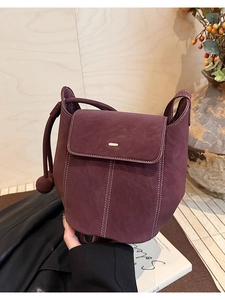 Détail du sac seau bordeaux avec surpiqûres blanches contrastées et pendentif boule en cuir