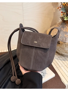 Détail d'un sac seau en cuir marron foncé avec coutures blanches et boucle dorée