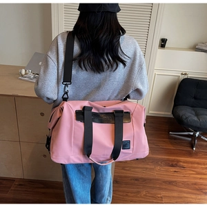 Pink nylon travel bag shown on a model in a minimalist home setting for size perspective