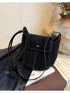 Détail du sac seau noir en daim avec surpiqûres blanches contrastées et pendentifs ronds