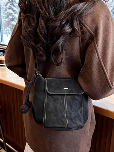 Sac seau noir minimaliste avec surpiqûres blanches sur un manteau en laine marron